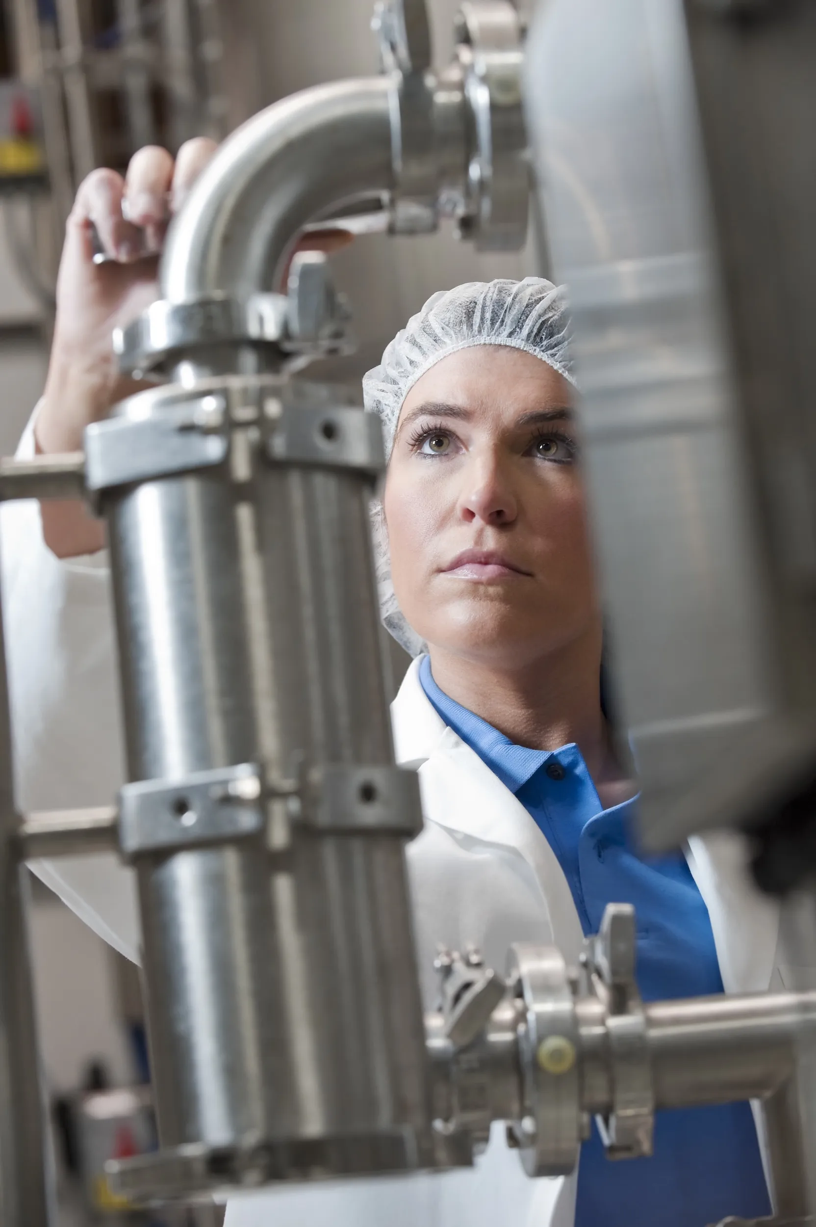 A technician in a lab coat and hairnet inspecting stainless steel dairy processing equipment